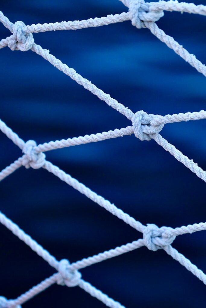 Detailed view of a fishing net with knots against a blurred blue sea background.